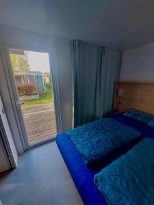 a bedroom with a blue bed and a large window at Mobil-home domaine la yole 5 étoiles in Vendres
