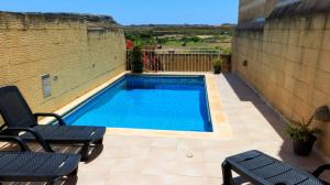 a swimming pool on a patio with two lounge chairs at Villa Ambrose Village in San Lawrenz