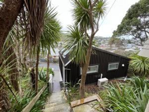 a black house with palm trees in front of it at Cosy, new, quiet Island Bay studio in Wellington