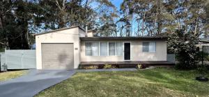 a white house with a garage in a yard at Waterfront Retreat by Book Jervis Bay Getaway Kayaks, Bikes, Fast Wi-Fi and more in Sanctuary Point
