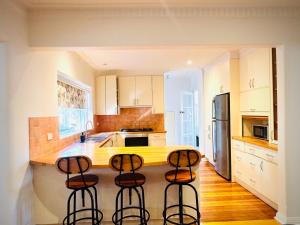 Cozy Beachside 5BR Home with Pool & Rumpus & King beds في ملبورن: مطبخ مع ثلاثة كراسي بار أمام منضدة