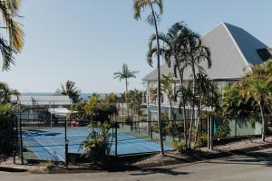 a tennis court with palm trees in front of a building at Pandanus Palms Ocean View Holiday Resort on Point Lookout in Point Lookout