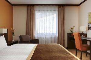 a hotel room with a bed and a desk and a window at Steigenberger Dortmund in Dortmund