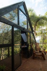 a glass house with a chair on a deck at Cabanas de Zorzi Refúgio na Natureza perto de Floripa in Santo Amaro da Imperatriz