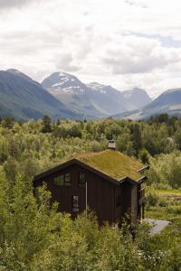 a building with a grass roof with mountains in the background at Nordic Luxury Apartment - Private Sauna & Panoramic Mountain Views in Stranda