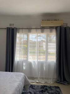 a bedroom with a bed and a window with curtains at Hillview Homes Apartment in Ndola