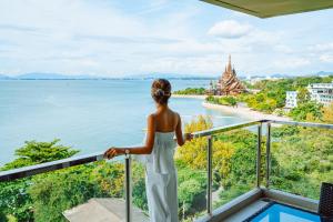 a woman standing on a balcony overlooking a body of water at Mayaana Beach Resort Pattaya - Formerly Golden Tulip Pattaya Beach Resort in North Pattaya