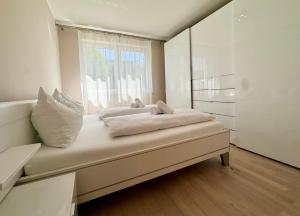 a white bedroom with a bed with a window at FAAKER SEE HIDEAWAY - Apartment mit Garten in Faak am See