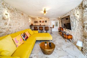a living room with a yellow couch and a stone wall at Luxury Villa Unikat with Seaview & Jacuzzi in Milna