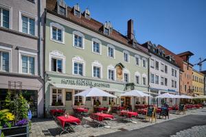 Un gran edificio con mesas y sombrillas en una calle. en Hotel & Gasthaus DAS RÖHRL Straubing, en Straubing