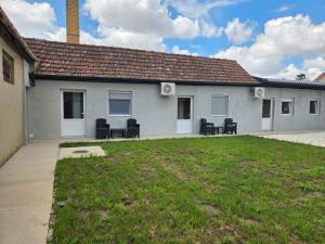a white building with chairs and a grass yard at Zolax Apartmans in Mali Iđoš