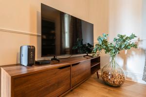 une télévision posée sur une commode en bois avec un vase dans l'établissement La Fine Bulle, Appartement de Charme au cœur de Reims, à Reims