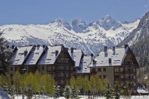 Un gran edificio con techos cubiertos de nieve frente a las montañas. en Apartarent 1500 - Apartamento Acebo, en Baqueira Beret