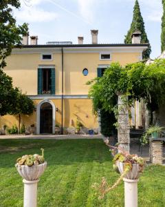 a large yellow house with two flower pots in the yard at Corte Pozzol in Rivoli Veronese