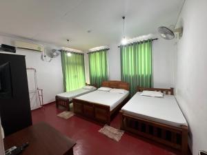 twee bedden in een kamer met groene gordijnen bij Nimsara Holiday Resort in Anuradhapura