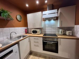 a kitchen with white cabinets and a sink and a microwave at Townhead Jewel by Coorie Doon Stays in Paisley +7 photos