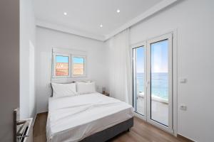a white bedroom with a bed and a large window at Blue Krathis - Luxury Seafront apartments in Paralía Akrátas