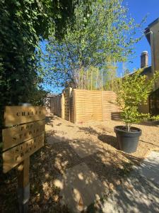 ein Schild in einem Garten mit einem Baum und einem Zaun in der Unterkunft Vinyle club-rétro 70's-6 pers-Terrasse-Wifi-Parking in Bellême