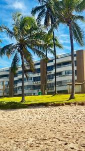 two palm trees in front of a building at Apto 2 quartos pé na areia com piscina Wi Fi e garagem em Vilas do Atlântico in Lauro de Freitas