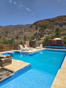 a swimming pool with chairs and a mountain in the background at casa rural LA LIMERA con piscina privada in Santa Lucía