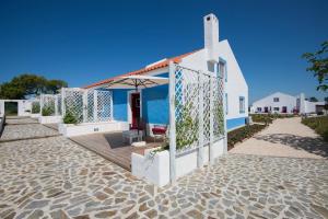 uma casa branca com um guarda-sol numa praia em Monte da Corça Nova em Vila Nova de Milfontes