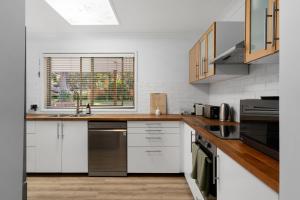 a kitchen with white cabinets and a sink and a window at Salt and Stone Modern Pearl Beach Stay 2 Mins to Ocean in Pearl Beach +19 photos