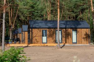 a wooden cabin with a black roof in the woods at Domki letniskowe w Centrum Rekreacji i Wypoczynkou Deczno in Sulnówko