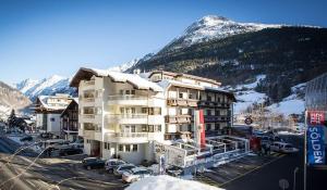 a building with a parking lot in front of a mountain at Hotel Valentin in Sölden