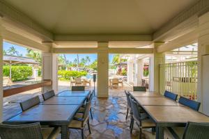 Un porche con mesas y sillas de madera en un patio. en Relax Unwind in Paradise The Islands K3, en Waikoloa
