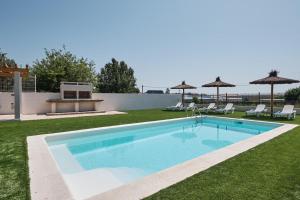 a swimming pool in a yard with chairs and umbrellas at As casiñas da Figueira by Serendipia Turismo in A Pobra do Caramiñal