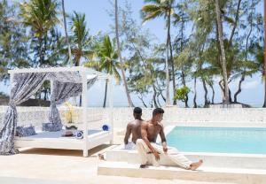 ブウェワウにあるZAN Orient Beach Hotelの二人の男性がプールの横に座っている