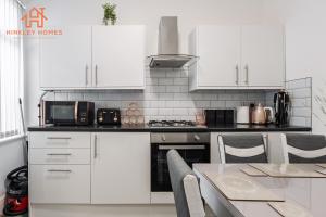 a kitchen with white cabinets and a table with chairs at 9 Guests, 4 Bedrooms, Modern Comfort in Bootle in Litherland