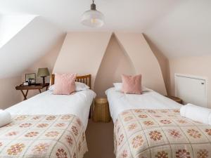 deux lits dans une chambre mansardée avec des murs blancs et des oreillers roses dans l'établissement Charming 2 Bed Cottage in the Heart of Adderbury Pass the Keys, à Adderbury