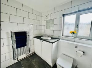 a white tiled bathroom with a sink and a toilet at Spacious 6 Bedroom House with Free Parking for Contractors and Business in Basildon