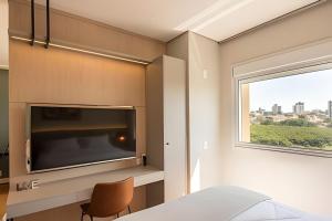 a living room with a large tv and a window at Charmoso Studio no Cambuí in Campinas