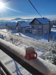 a cup of coffee sitting on a rail in the snow at N&M Mountain Escape in Kupres