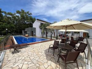 a patio with a table and umbrella next to a pool at 400m da Praia | Roupa de cama/banho in Pauba