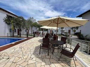 a patio with a table and umbrella next to a pool at 400m da Praia | Roupa de cama/banho in Pauba