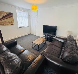 a living room with a leather couch and a flat screen tv at Millhouse 55 in Risca