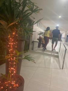due persone che camminano lungo un corridoio con una pianta con luci di Hotel Enseada dos Corais a Cabo de Santo Agostinho