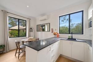a kitchen with white cabinets and a table and two windows at Hunter Valley Prime Getaway in Pokolbin