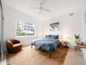a white bedroom with a bed and a chair at The Fletcher Bondi in Sydney