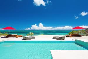 a swimming pool with chairs and umbrellas on the beach at Beachfront luxury 2 bedroom villa on Grace Bay in Providenciales