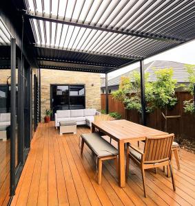 ニュープリマスにあるLuxury Fitzroy Beach Retreatの木製パティオ(木製テーブル、椅子付)