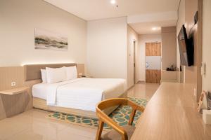 a bedroom with a white bed and a chair in it at Skysuites Residence Surabaya in Kedungbaruk