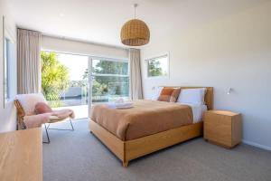a bedroom with a bed and a chair and a window at Kiwi Street Retreat in Waiheke Island +15 photos