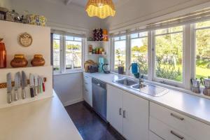 - une cuisine avec des comptoirs et des fenêtres blancs ainsi qu'un évier dans l'établissement Driftwood Cottage, à Waiheke Island 13 autres photos