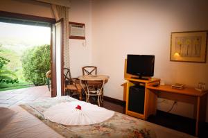 a room with a bed and a television and a table at Canto da Floresta Ecoresort in Amparo