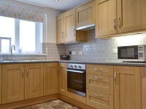a kitchen with wooden cabinets and a stove top oven at The Birches in Keswick +21 photos