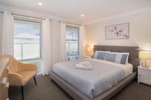 a bedroom with a bed and a chair and windows at Dunsborough Sunrise in Dunsborough